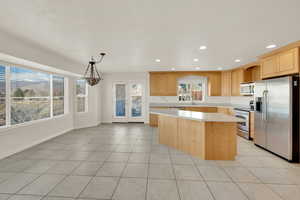 Kitchen with stainless steel appliances, decorative light fixtures, a center island, and light brown cabinets