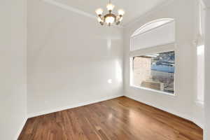 Empty room with an inviting chandelier, hardwood / wood-style floors, and crown molding