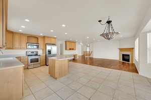 Kitchen with light tile patterned flooring, a kitchen island, appliances with stainless steel finishes, pendant lighting, and light brown cabinetry