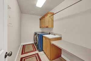 Washroom featuring sink, cabinets, light tile patterned floors, independent washer and dryer, and a textured ceiling