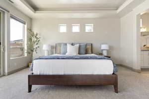 Bedroom featuring light carpet, ensuite bath, and a tray ceiling