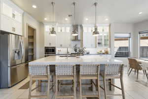 Kitchen featuring white cabinets, hanging light fixtures, stainless steel appliances, a center island with sink, and wall chimney exhaust hood