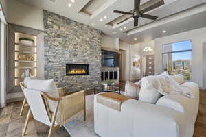 Living room featuring a fireplace, ceiling fan with notable chandelier, light hardwood / wood-style flooring, and a raised ceiling