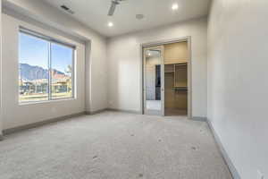 Unfurnished bedroom with a walk in closet, ceiling fan, a mountain view, light carpet, and a closet