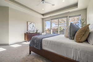 Carpeted bedroom featuring ceiling fan and a tray ceiling