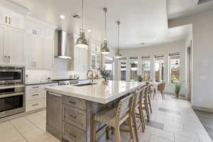 Kitchen with sink, white cabinetry, stainless steel appliances, an island with sink, and wall chimney exhaust hood