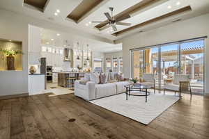 Living room featuring ceiling fan, a tray ceiling, a high ceiling, and light wood-type flooring