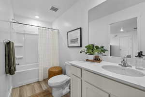 Full bathroom with shower / bathtub combination with curtain, hardwood / wood-style floors, vanity, and toilet