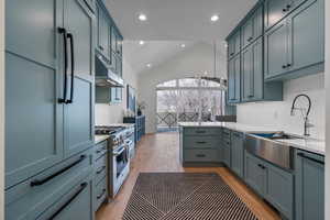 Kitchen featuring sink, refrigerator, vaulted ceiling, light hardwood / wood-style flooring, and stainless steel stove