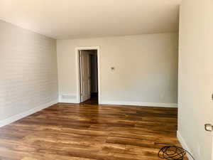 Unfurnished room featuring brick wall and dark hardwood / wood-style flooring