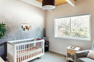 Carpeted bedroom with a nursery area, beam ceiling, and wooden ceiling