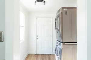 Laundry area featuring stacked washer and clothes dryer and light hardwood / wood-style flooring