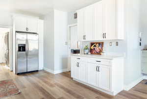 Kitchen with white cabinetry, stacked washing maching and dryer, stainless steel fridge, and light hardwood / wood-style flooring