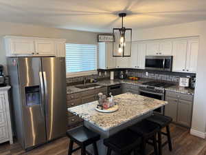 Kitchen with sink, appliances with stainless steel finishes, a kitchen island, pendant lighting, and light stone countertops