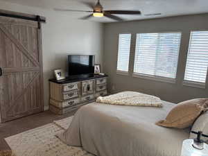 Carpeted bedroom with multiple windows, a barn door, and ceiling fan