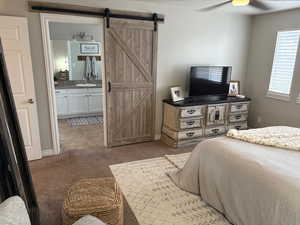 Carpeted bedroom featuring ceiling fan, ensuite bathroom, a barn door, and sink