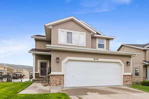 View of front facade with brick siding, stucco siding, an attached garage, concrete driveway, and a front lawn