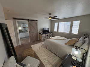 Carpeted bedroom featuring ensuite bathroom, sink, a textured ceiling, ceiling fan, and a barn door