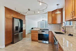 Kitchen with sink, vaulted ceiling, hanging light fixtures, stainless steel appliances, and light stone countertops