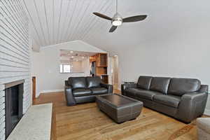 Living room with lofted ceiling, wood ceiling, ceiling fan, a fireplace, and light wood-type flooring