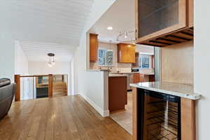 Kitchen featuring decorative light fixtures, beverage cooler, decorative backsplash, kitchen peninsula, and light stone countertops