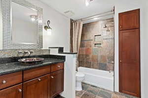 Full bathroom featuring vanity, decorative backsplash, shower / bath combination with curtain, and toilet