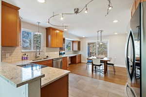 Kitchen featuring appliances with stainless steel finishes, decorative light fixtures, sink, kitchen peninsula, and light stone countertops