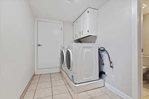 Washroom with cabinets, washing machine and dryer, and light tile patterned floors