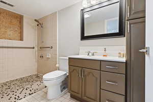 Bathroom with vanity, a tile shower, tile patterned floors, and toilet