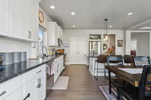 Kitchen with sink, white cabinetry, hanging light fixtures, stainless steel appliances, and dark hardwood / wood-style flooring