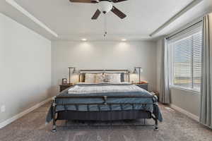 Carpeted bedroom with ceiling fan, a raised ceiling, and a textured ceiling