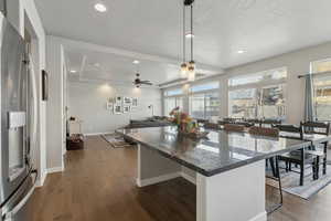 Kitchen featuring dark wood-type flooring, a breakfast bar area, decorative light fixtures, stainless steel fridge with ice dispenser, and a textured ceiling