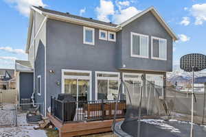 Snow covered rear of property with a trampoline, central AC, and a deck with mountain view