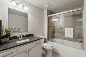 Full bathroom with enclosed tub / shower combo, vanity, a textured ceiling, tile patterned floors, and toilet