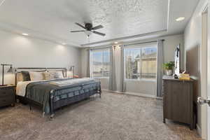 Carpeted bedroom with ceiling fan, a textured ceiling, and a tray ceiling