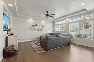 Living room featuring ceiling fan, a textured ceiling, dark hardwood / wood-style flooring, and a tray ceiling