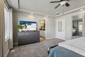 Carpeted bedroom with connected bathroom, a raised ceiling, and ceiling fan