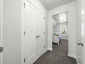 Corridor featuring dark colored carpet, lofted ceiling, and a textured ceiling