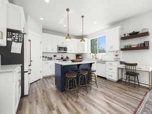 Kitchen featuring refrigerator, decorative light fixtures, dishwasher, a breakfast bar area, and white cabinets