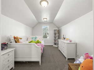 Bedroom featuring dark carpet, vaulted ceiling, and a textured ceiling