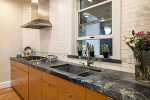 Kitchen with wall chimney range hood, sink, tasteful backsplash, light hardwood / wood-style floors, and dark stone counters