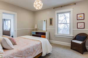 Carpeted bedroom featuring multiple windows and an inviting chandelier