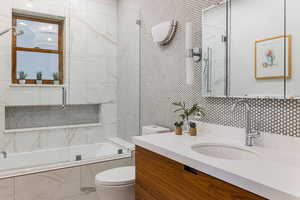 Full bathroom featuring vanity, toilet, tiled shower / bath combo, and tile walls