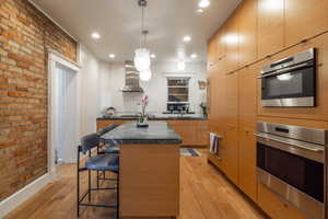 Kitchen featuring wall chimney exhaust hood, a kitchen bar, a kitchen island, pendant lighting, and light hardwood / wood-style floors