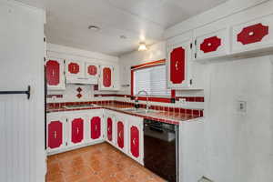 Kitchen with tile counters, black dishwasher, sink, and white cabinets