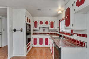 Kitchen featuring white cabinetry, sink, backsplash, tile counters, and black appliances