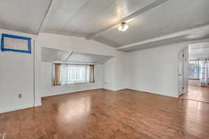 Empty room featuring hardwood / wood-style flooring and vaulted ceiling with beams