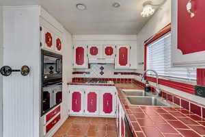 Kitchen featuring sink, black appliances, tile counters, decorative backsplash, and white cabinets