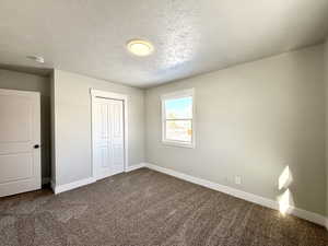 Unfurnished bedroom featuring carpet, a textured ceiling, and a closet