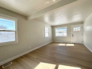 Entrance foyer with beam ceiling, light hardwood / wood-style floors, and a textured ceiling